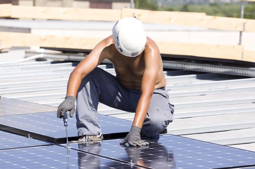 Ein Arbeiter montiert Solarpanele auf einem sonnigen Flachdach